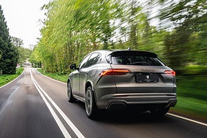 En Maserati SUV kör bort längs en slingrande landsväg omgiven av gröna träd.