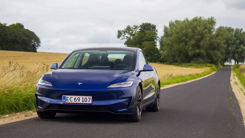 En mörkblå Tesla Model 3 fotograferad framifrån på en landsväg