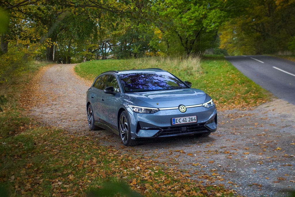 En grå volskwagen id.7 kör längs en smal skogsväg kantad av höstlöv.