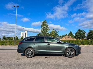 Sidovy av en grön Hyundai i30 parkerad utomhus, med blå himmel i bakgrunden.