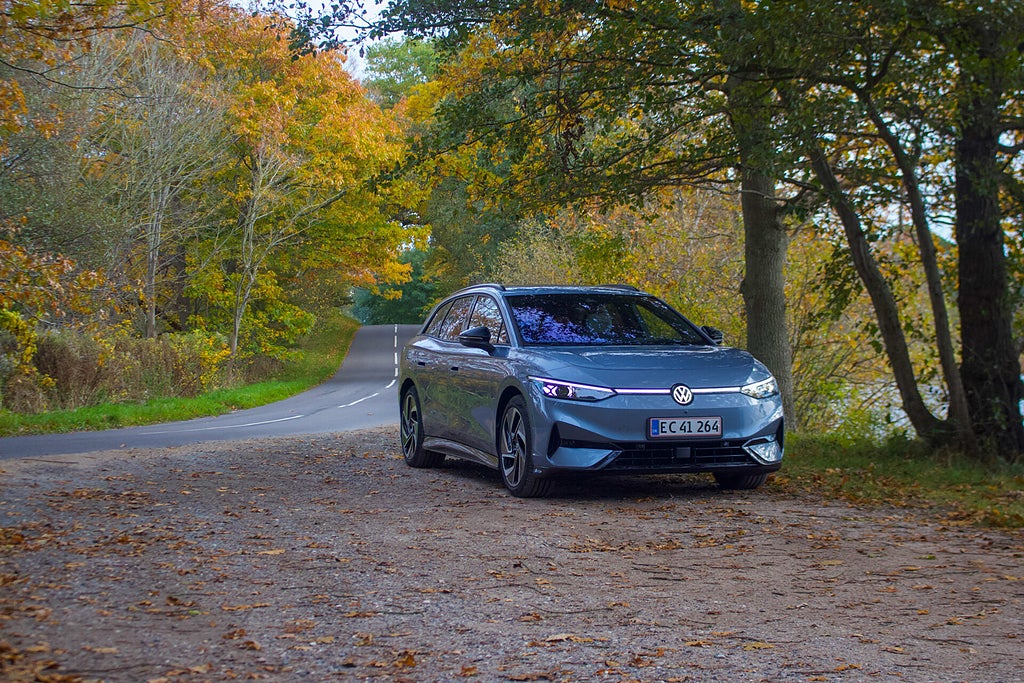 Framsidan av bilen parkerad på en grusväg med höstträd i bakgrunden.
