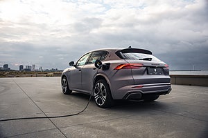 En Maserati SUV laddas, med en lång kabel ansluten och en stadssilhuett i bakgrunden.