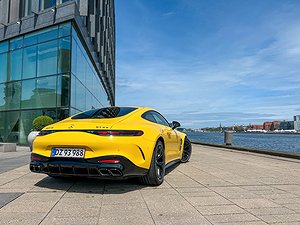 Bakre sidan av en gul Mercedes-AMG GT vid en glasbyggnad på en kaj.