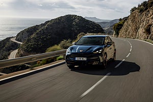 Svart Cupra kör på en slingrande kustväg med havet och bergen i bakgrunden.