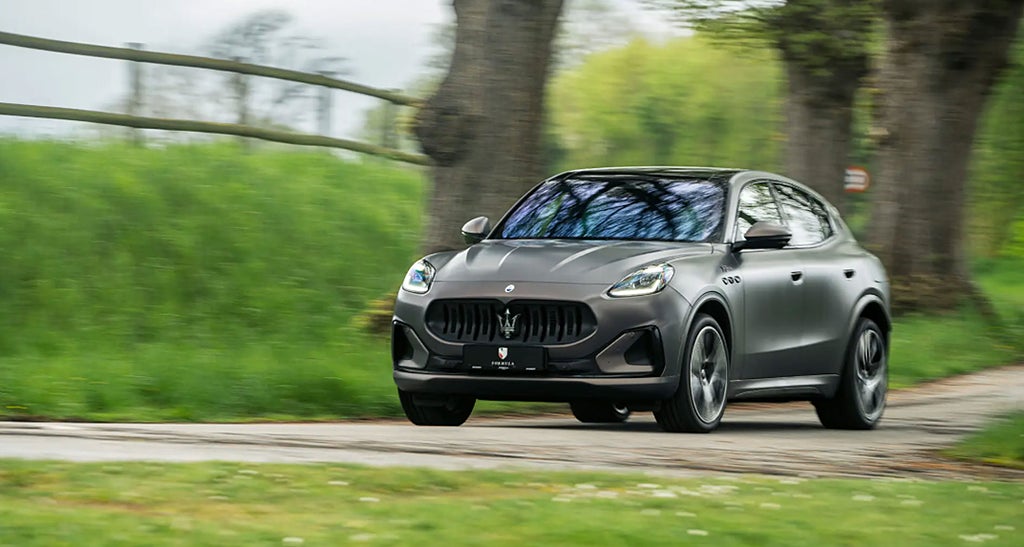 En Maserati SUV kör på en landsväg med gröna träd och gräs i bakgrunden.