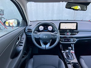 Förarens vy av interiören i en Hyundai-bil, inklusive ratt, instrumentpanel och mittkonsol med skärm och knappar.