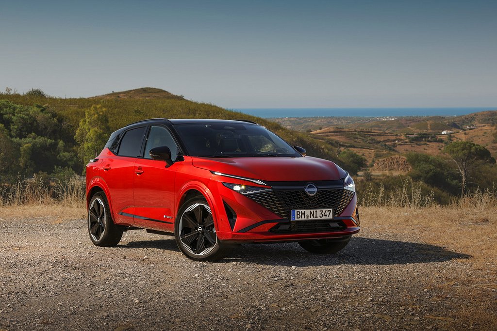 En röd Nissan Qashqai parkerad på en grusväg med landskap och hav i bakgrunden.