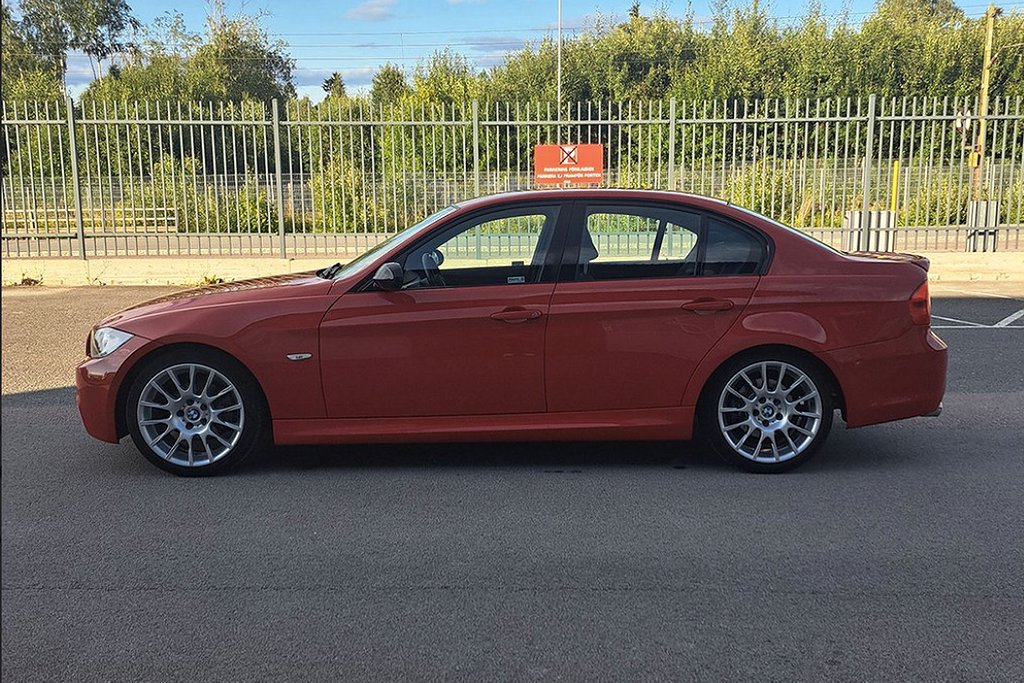 Röd BMW sedan parkerad vid ett staket med grönska i bakgrunden.