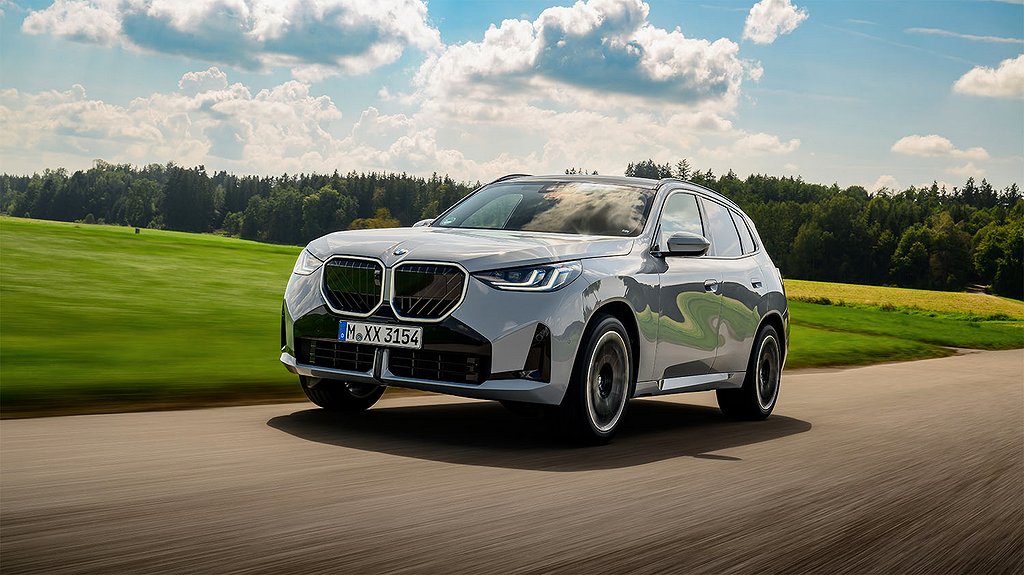 Bakifrån vy av en BMW SUV som kör på en landsväg genom grönt landskap.